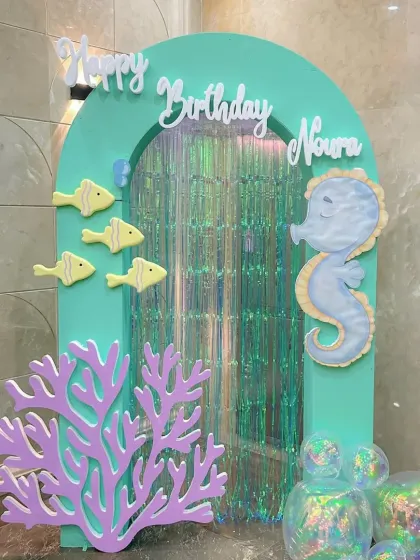 A whimsical entrance arch for a mermaid party, featuring a seahorse, little fish, and an iridescent curtain for a magical entry.