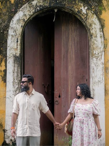 A classic portrait of the couple holding hands in front of a large, rustic wooden door in Goa. The textures and colors of the location add a vintage charm.