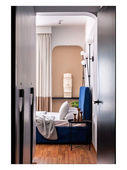 A glimpse into another bedroom, where a deep blue velvet bed is framed by an arched doorway. The design uses muted tones and a tasteful palette of art to create a warm and inviting atmosphere.