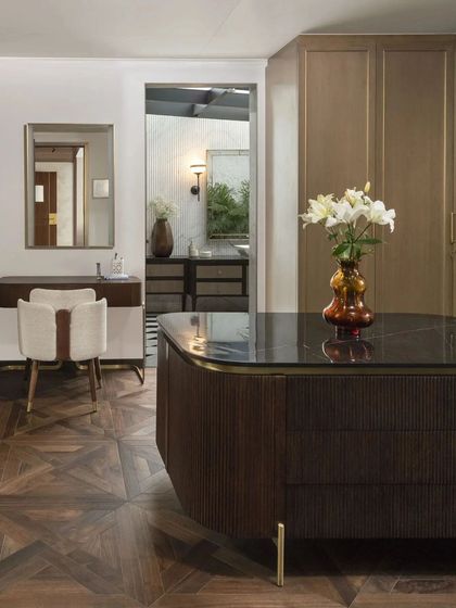 A walk-in closet and dressing area featuring a central island with a dark stone top and ribbed wood detailing. The design combines engineered wood flooring with custom cabinetry for a highly functional and luxurious space.