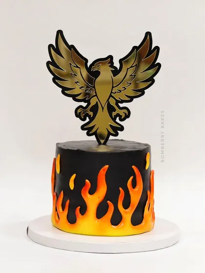 A striking Phoenix cake, with a black base, fiery orange and yellow flames, and a bold golden phoenix topper.
