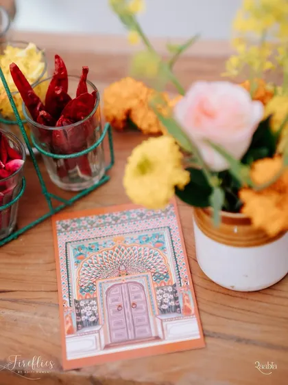 A close-up of the stationery and table decor for the 'Jaipur Wali Haldi'. The invitation card features a beautiful illustration of a Rajasthani door, complemented by fresh marigolds and spices.