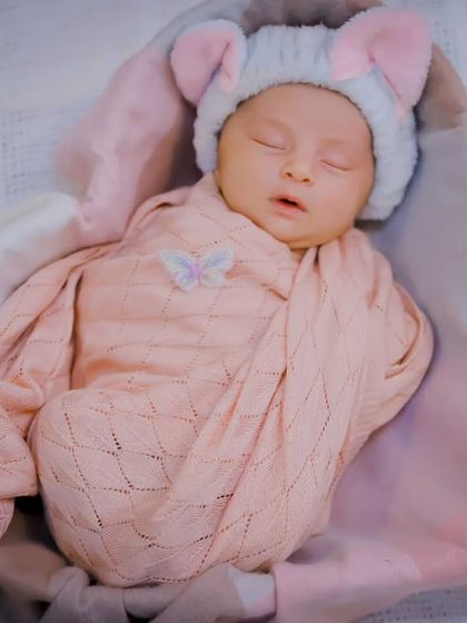 A sleeping newborn girl, snug in a pink swaddle with a cute mouse-ear hat. We use soft wraps and adorable accessories to create sweet, peaceful portraits.