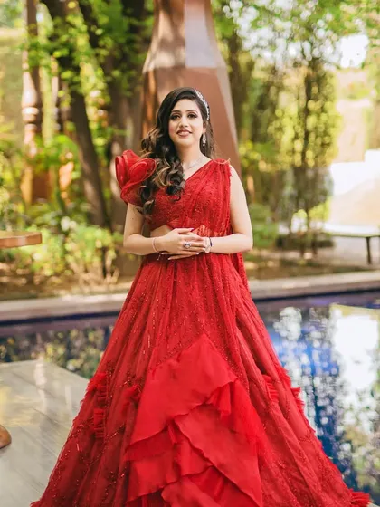 A full-length shot of the bride by the pool. Her makeup is flawless, and her bold red lehenga makes a stunning statement.