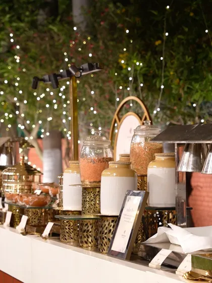 A beautifully arranged buffet station under a canopy of fairy lights, featuring traditional Indian martabans and elegant serveware.