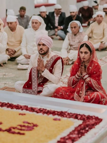 A wide shot of the couple seated before the Guru Granth Sahib, showing the full context of the sacred Anand Karaj ceremony.