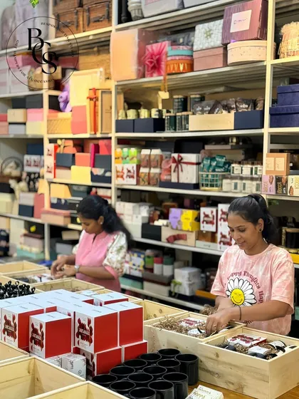 A wide shot of our bustling studio. You can see our shelves stocked high with boxes and supplies, and our team members diligently working on assembling various hamper orders. This is where the creativity happens.