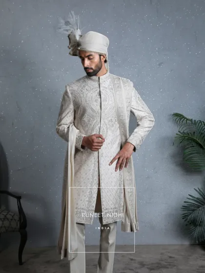 Crafted in a luxurious ivory silk base, this sherwani is adorned with intricate resham embroidery. Elaborate paisley and floral patterns grace the chest and shoulders, creating an heirloom of elegance.