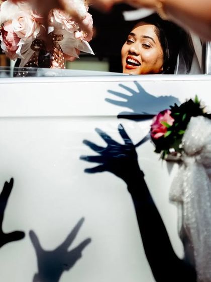 A playful shot of the bride in her car, with the shadows of her friends' hands waving at her.