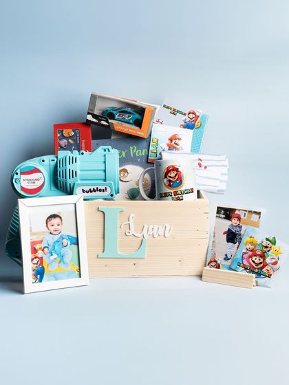 The full Super Mario birthday hamper, overflowing with fun toys, a personalized mug, photos, and a bubble gun, all in a custom-monogrammed wooden box.