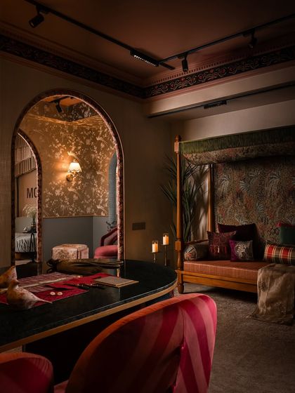 A moody, atmospheric shot of the client interaction zone. The custom daybed, upholstered in a rich botanical print, sits opposite the curved desk, creating a luxurious yet comfortable space for conversation and collaboration.