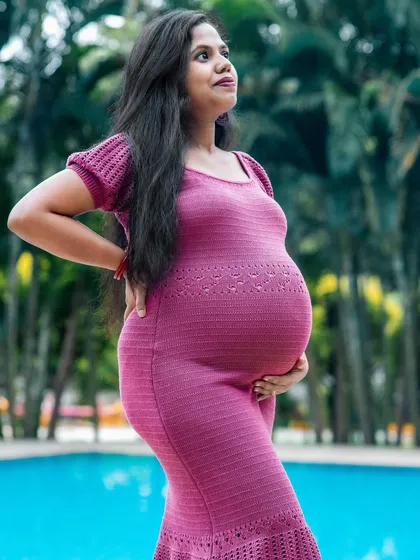 This portrait highlights the beautiful silhouette of pregnancy. The form-fitting magenta dress and the simple poolside setting create a modern and striking maternity image.