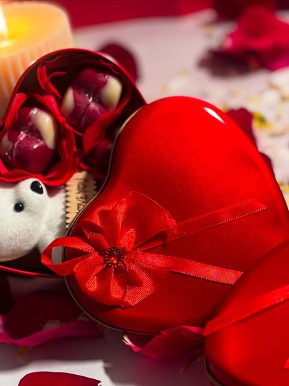 A romantic Valentine's gift option featuring a heart shaped tin filled with handmade chocolates and a small teddy bear. It's a sweet and simple way to show your love.