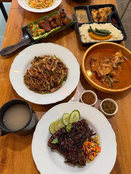 A closer look at a portion of our feast, featuring pork ribs, a chicken curry, noodles, and a packed meal box, showing options for both dine-in and takeaway.