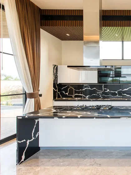 A close-up of the kitchen island, made from a single piece of black marble with dramatic white veining. The island incorporates a cooktop, making it a central hub for cooking and socializing.