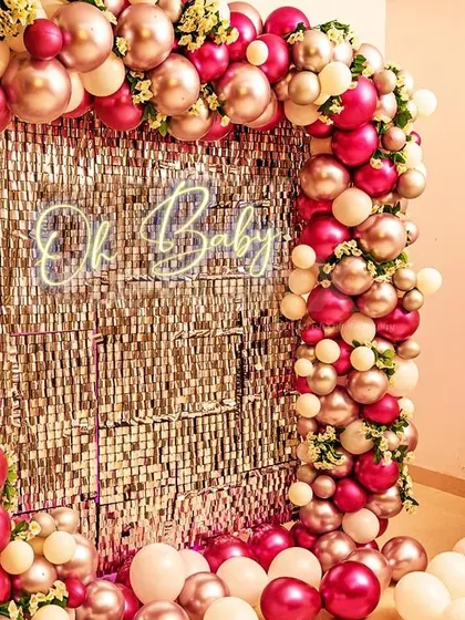 A glamorous 'Oh Baby' shower decoration with a silver sequin wall. The backdrop is framed by a stunning arch of metallic pink and cream balloons.