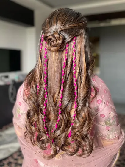 For a fun Haldi or Mehendi party, I love adding a pop of color. This half-up style features a rose bun and playful pink braids woven into soft curls, perfectly matching the fun and festive vibe of the event.