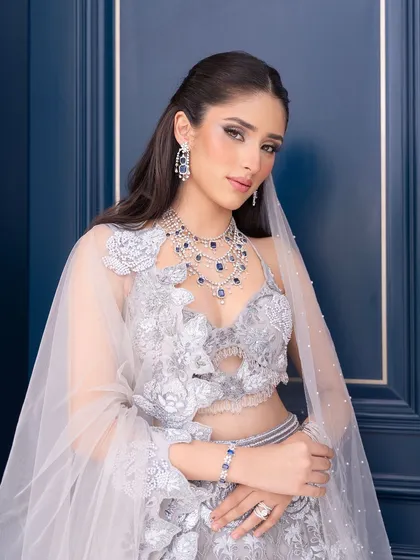 A modern and chic bridal portrait. The makeup is clean and sophisticated, with a focus on sculpted features and a radiant complexion that glows against the deep blue background.
