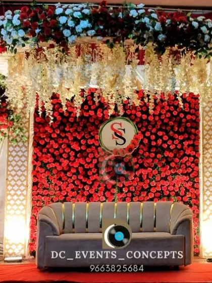 A classic and romantic wedding reception stage, enveloped in a wall of rich red roses and elegant white florals. The dramatic draping and warm lighting create an atmosphere of pure romance.
