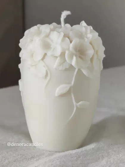 A taller, vase-shaped floral pillar candle with intricate flowers and vines.
