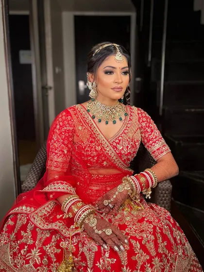 A full-length view of Krisha's stunning bridal attire, with makeup designed to complement the rich red and intricate embroidery of her lehenga.