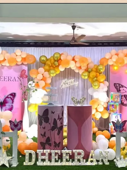 An orange and gold butterfly theme decoration. The setup includes a white picket fence and large, colorful butterfly cutouts.