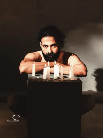 A powerful and intense portrait, leaning over a collection of lit candles. The composition is symmetrical and strong, with his gaze drawing you directly into the scene.