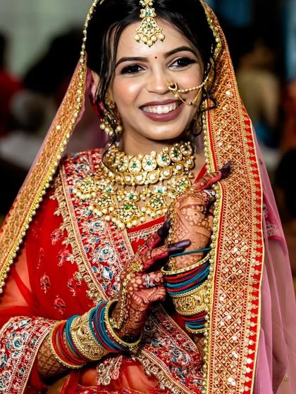 A radiant bride showcasing her complete look. The detailed Kundan work on the necklace and the delicate nath perfectly frame her face, highlighting her joy.
