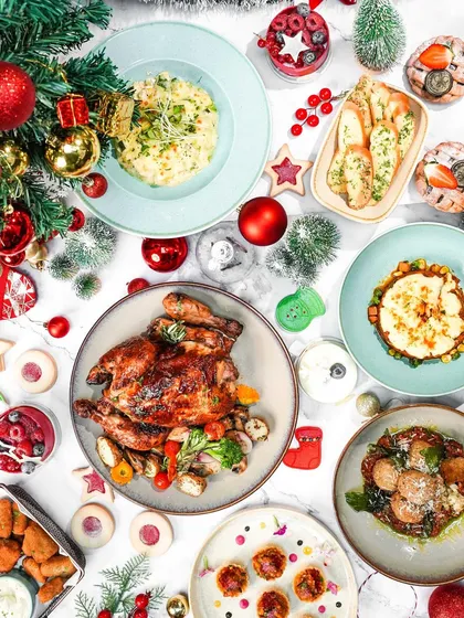 A flatlay of a Christmas brunch spread, featuring a whole roasted chicken and various side dishes. The festive decorations scattered around create a joyful and abundant holiday table.