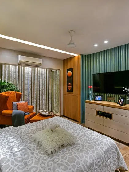 This bedroom features a vibrant mix of colors and textures, with a teal fluted wall, an orange armchair, and wooden paneling. The design creates a cheerful and energetic yet comfortable personal space.