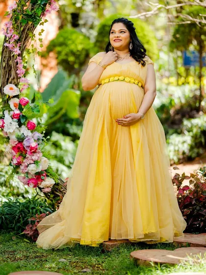 A radiant mom-to-be in a flowing yellow gown, framed by a rustic floral arch. The soft lighting and cheerful colors create a picture of pure happiness.
