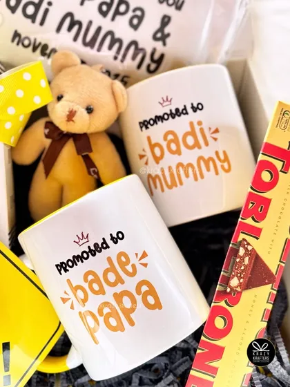 A close-up of the 'Promoted to Bade Papa & Badi Mummy' mugs from a family announcement hamper. It's a wonderful way to make extended family feel part of the celebration.