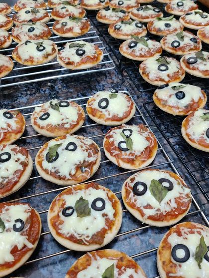 A batch of our mini pizzas fresh out of the oven. These bite-sized treats are perfect for parties, topped with our homemade tomato sauce, mozzarella cheese, basil, and a black olive.