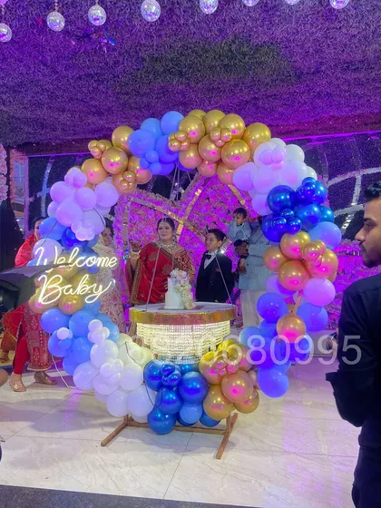 For a grand welcome baby celebration at a banquet hall, I created this large ring backdrop with blue, white, and gold balloons. The setup includes a 'Welcome Baby' neon sign and a central cake table, making it a stunning focal point for the event.