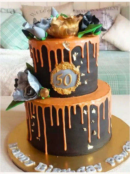 A bold two-tier cake in black and orange with a drip effect and floral toppers for a 50th birthday.