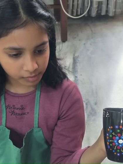 A young artist concentrating on the final touches of her dot mandala mug painting.