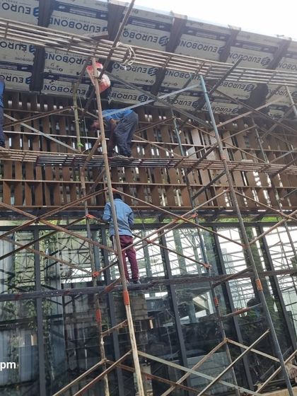 Workers on scaffolding, completing the installation of the upper facade and roof cladding of the Experience Center.