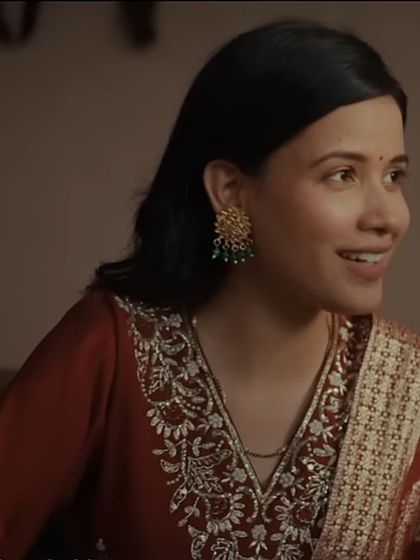 A close-up on the actress from the 'Jaago Janani' project. The intricate embroidery on her red suit and the traditional earrings were chosen to create a look that is both beautiful and authentic for a family setting.