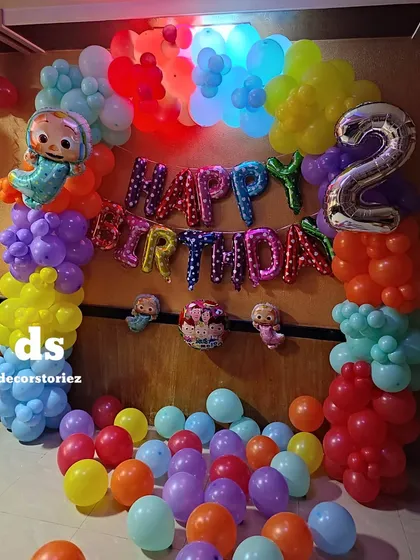 Another view of the Cocomelon party decor, showcasing the colorful 'Happy Birthday' foil balloons and the arrangement of character cutouts.