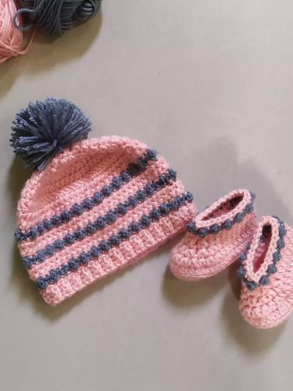The Dewdrops beanie and booties set, shown together. The beanie features a fluffy pom-pom, and the booties have a matching design, creating a perfect gift set for a new baby.