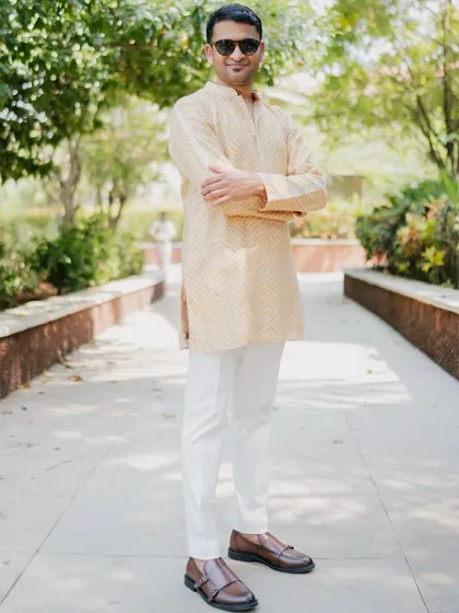 The groom looking cool and casual in a subtle yellow bandhani print kurta, perfectly complementing the bride's welcome outfit.