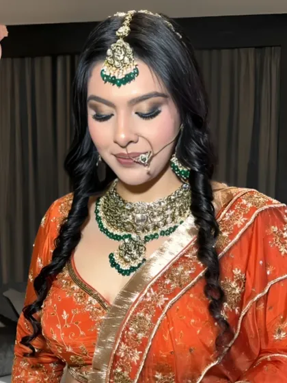 A close-up of the reception bride in her orange lehenga. The makeup features a smokey eye and a neutral lip, perfectly balancing the vibrant outfit.