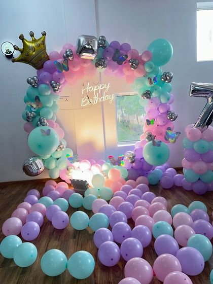 This butterfly and princess theme decoration uses a pastel balloon ring arch. I added butterfly cutouts, a crown foil balloon, and a large number '7' pillar for the birthday girl.