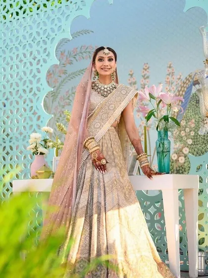 A beautiful bride in her pastel lehenga, posing against the elegant decor. The design features a custom jaali screen and a soft color palette that enhances her ethereal look.