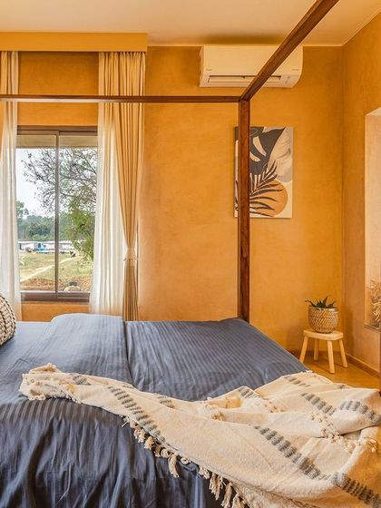 This bedroom is a cocoon of warmth, with earthy lime-plastered walls and a classic four-poster bed made of dark wood. The bay window seat offers a cozy nook for reading while enjoying views of the outdoors.