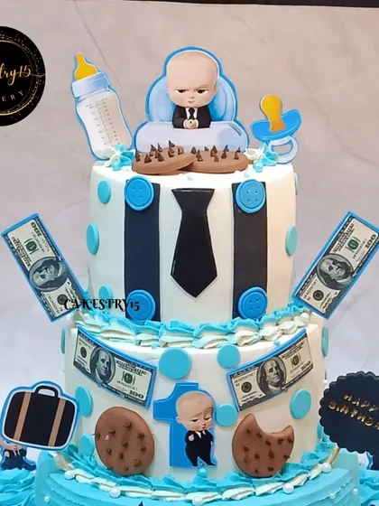A close-up of the top two tiers of the Boss Baby twins' cake, showing the detailed fondant work including a tie, cookies, and edible money.