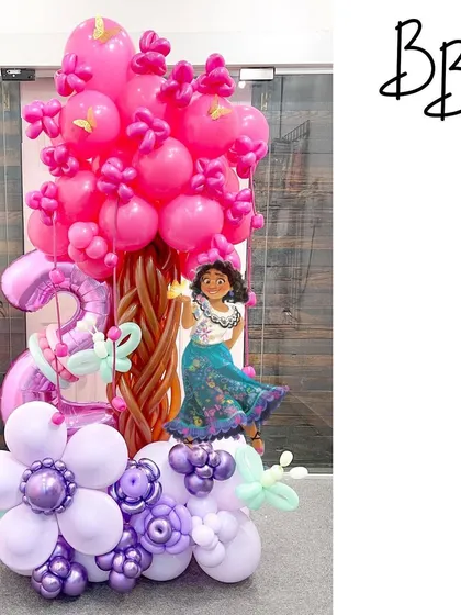 A magical Encanto-themed display for a 3rd birthday. This piece features Mirabel next to a vibrant pink balloon tree and purple balloon flowers, capturing the enchanting spirit of the movie.
