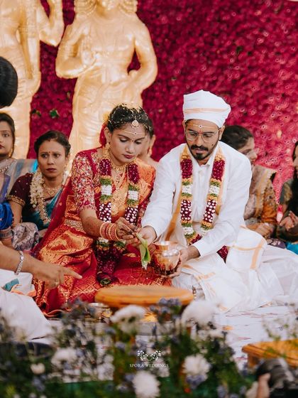 The couple performing a ritual together, surrounded by flowers and in front of golden deities, a truly grand setting.