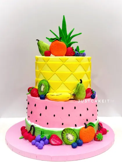 A "tutti frutti" two-tier cake, where the tiers themselves look like a pineapple and a watermelon. The cake is adorned with a variety of hand-molded, edible fruits.