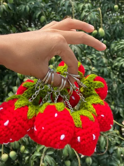 Holding a bunch of strawberry keychains to show the secure metal rings. They are ready to be attached to bags, keys, and more.